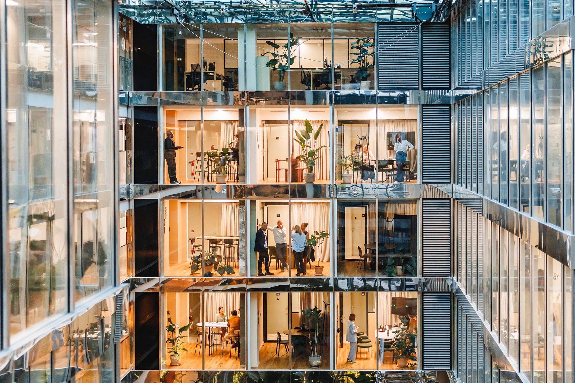 Men and women of various backgrounds collaborate and work independently in a spacious, well-lit office setting, each attired suitably for a professional setting, using modern tools and technology.